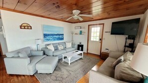 A living room with a grey sectional sofa, a white coffee table, a grey rug, a ceiling fan, a flat-screen TV, and a wooden ceiling. - Discover Sea La Vie: an oceanfront 3-bedroom haven in Surf City, perfect for families! (Surf City)