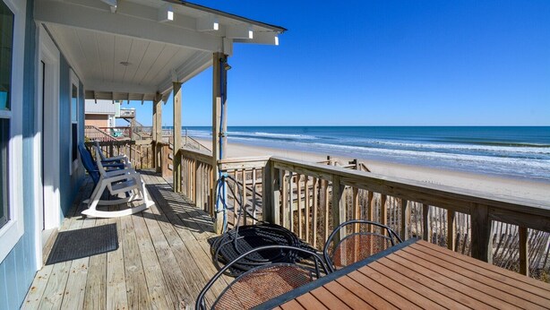 A wooden deck with beach chairs and a table overlooking the ocean. - Discover Sea La Vie: an oceanfront 3-bedroom haven in Surf City, perfect for families! (Surf City)
