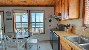 A kitchen with wooden cabinets, a stove, and a sink. There is a dining table with chairs and a view of the ocean through the windows. - Discover Sea La Vie: an oceanfront 3-bedroom haven in Surf City, perfect for families! (Surf City)