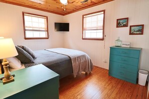 Una camera da letto con un letto, una cassettiera, una TV e due finestre.
