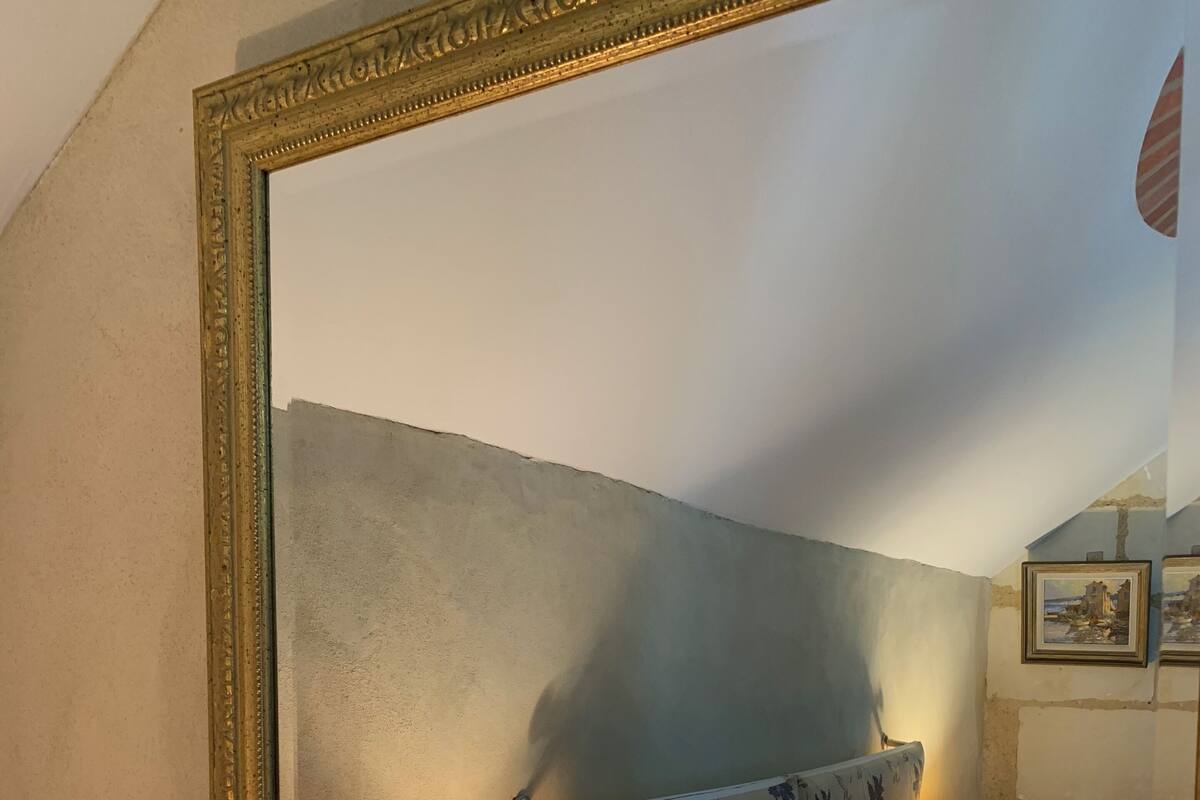 A bedroom with a bed, a nightstand with a lamp, a large mirror, and a wall with a floral pattern.