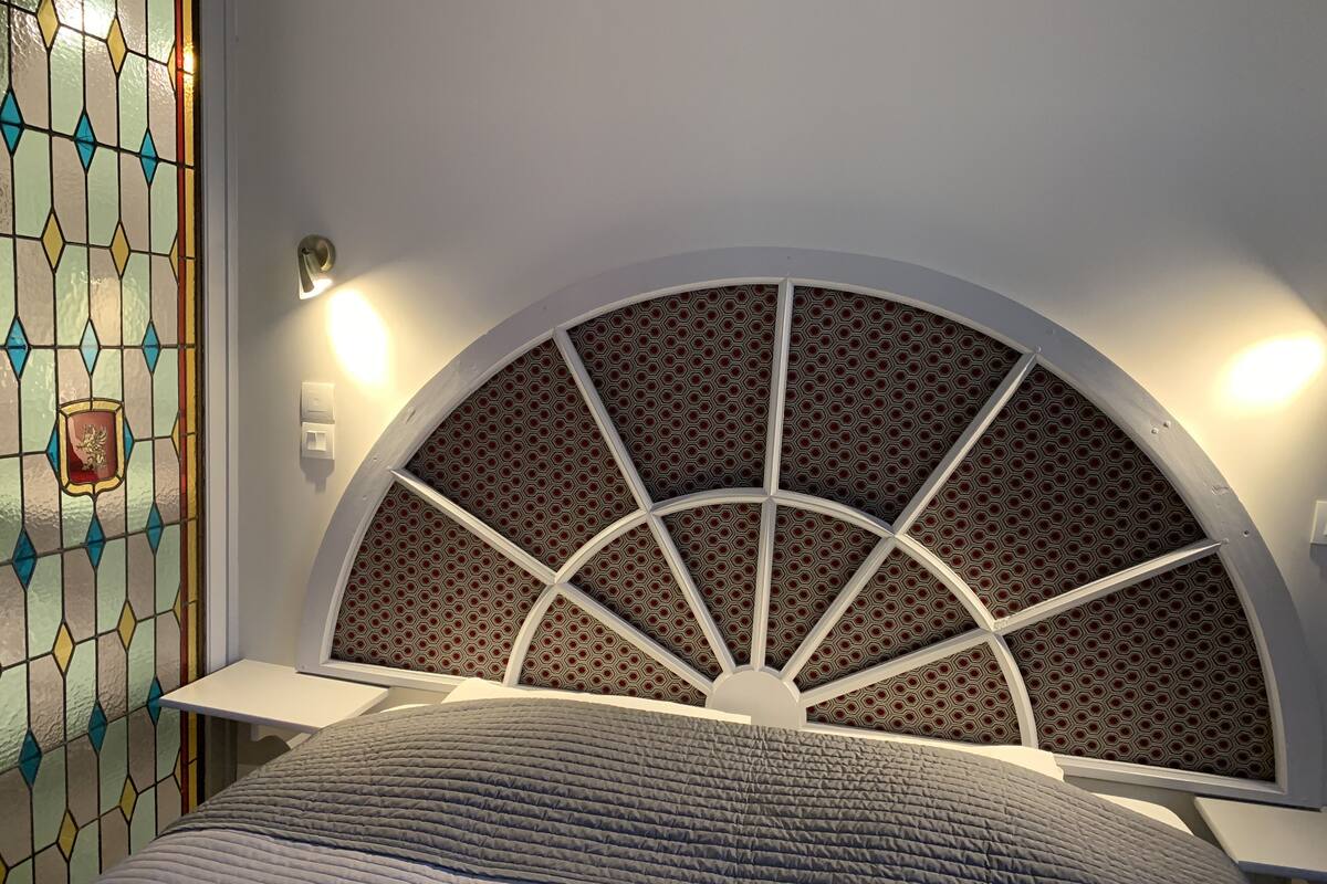 A bedroom with a bed, a decorative headboard, and a stained glass window.