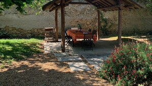 A rustic outdoor seating area with a wooden pergola, stone wall, and a gravel path leading to a table and chairs. - Clos des 3 Rois Chambres Hôtes Thouarcé (Bellevigne-en-Layon)
