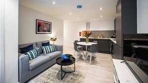 Una sala de estar moderna con un sofá gris, una mesa de centro y un comedor con una mesa y sillas blancas.