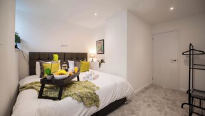 Un dormitorio ordenado con cama, mesita de noche y perchero.