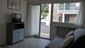 A room with a sofa, a television on a cabinet, and a sliding glass door leading to an outdoor area. - STUDIO 400 M FROM THE OCEAN TERRACE, PARKING AND BIKE SHELTER AVAILABLE (La Rochelle)