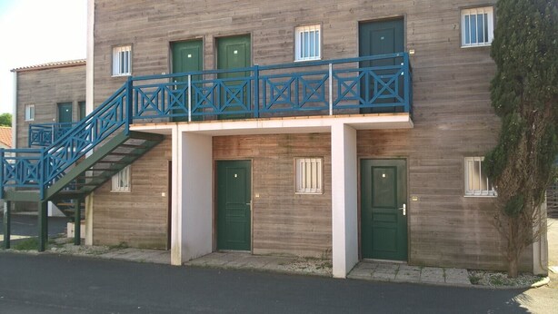 A two-story building with a blue staircase leading to a balcony, green doors, and a small window on the ground floor. - STUDIO 400 M FROM THE OCEAN TERRACE, PARKING AND BIKE SHELTER AVAILABLE (La Rochelle)