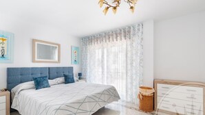 Een slaapkamer met een bed, nachtkastje, kapstok, spiegel en een raam met gordijnen.