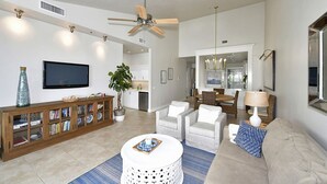 A spacious living room with a flat-screen TV, a wooden entertainment unit, a ceiling fan, and a dining area with a chandelier. - Beautiful bayfront view! December 2026 dates available now! (Longboat Key)