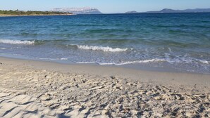 A beach with clear blue water, sandy shore, and distant mountains.