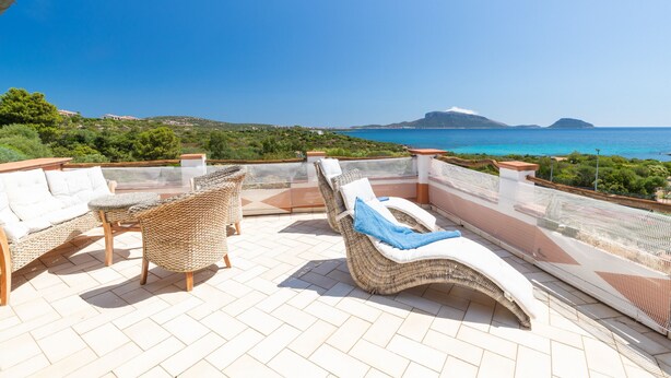 A rooftop terrace with wicker furniture, a view of the sea, and a distant mountain.