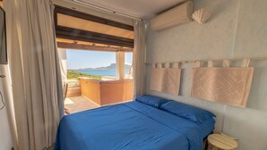 A bedroom with a large bed, a small stool, and a view of the sea.