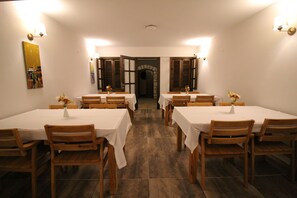 A dining area with multiple tables and chairs, a tiled floor, and a doorway leading to another room. - Green House Bozcaada (Bozcaada)