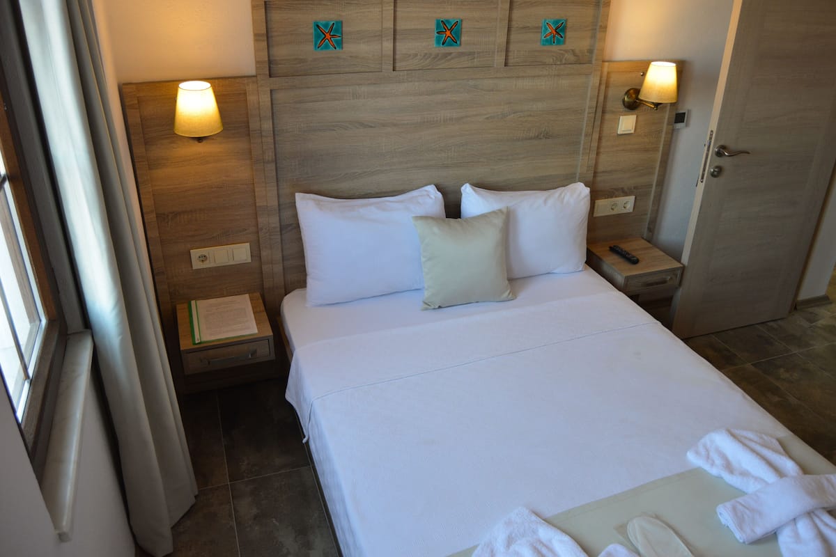 A hotel room with a large bed, two bedside lamps, a wooden headboard, and a door.