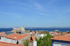 A coastal town with terracotta-roofed buildings, a historic fort, and a view of the sea and distant bridges. - Green House Bozcaada (Bozcaada)