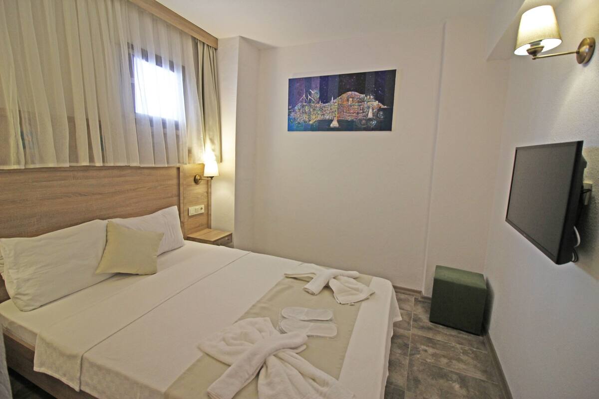 A hotel room with a bed, a nightstand, a TV, and a painting on the wall.