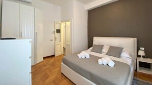 A modern bedroom with a large bed, a bedside table, a nightstand, and a wardrobe.
