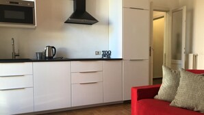 A modern kitchen with white cabinets, a black range hood, and a red sofa in the living area.