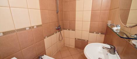 Un baño con ducha, dos lavamanos y un inodoro.