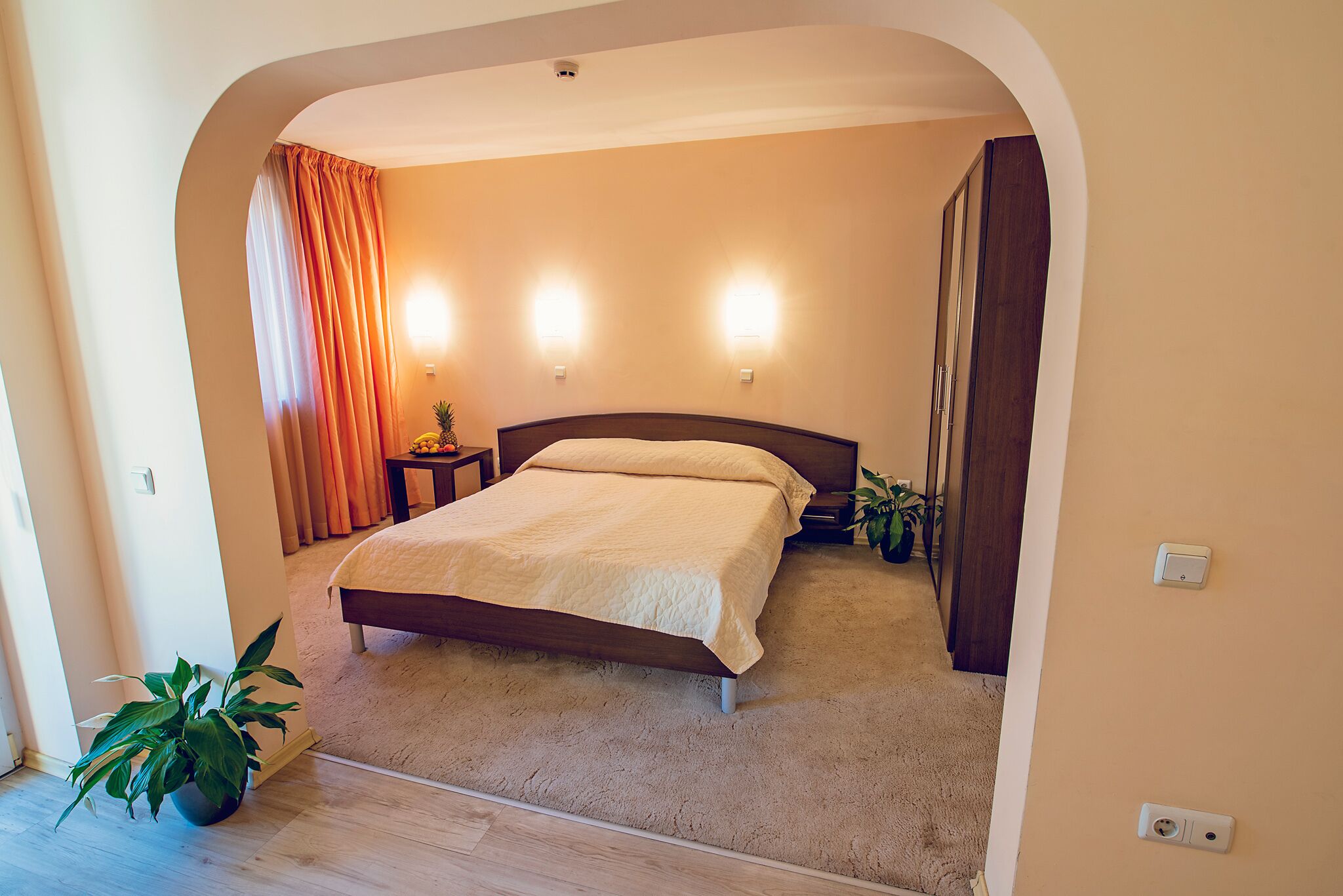 A bedroom with a bed, bedside tables, a potted plant, and a curtain.