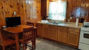 Cocina con paneles de madera, una mesa de comedor, sillas, estufa y lavaplatos.