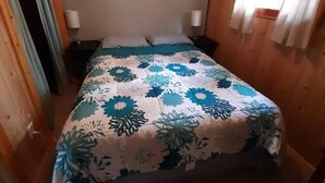 Una habitación con cama, un cuadro en la pared y una ventana con cortinas.