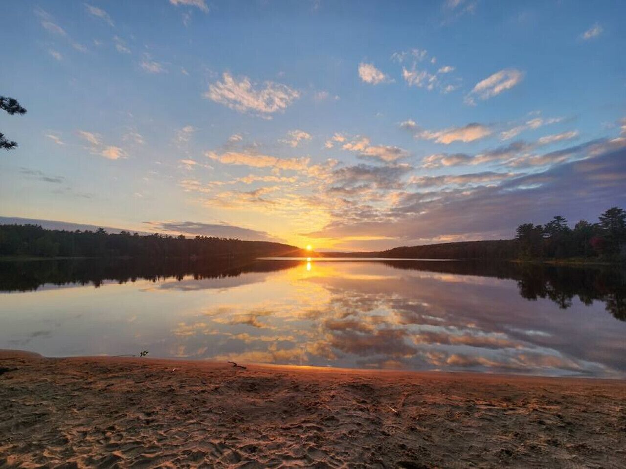 Un lac paisible au coucher du soleil, avec un ciel dégagé et des arbres qui se dessinent à l’horizon.