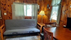 Interior de una cabaña de madera con sofá, una mesa de comedor y sillas.