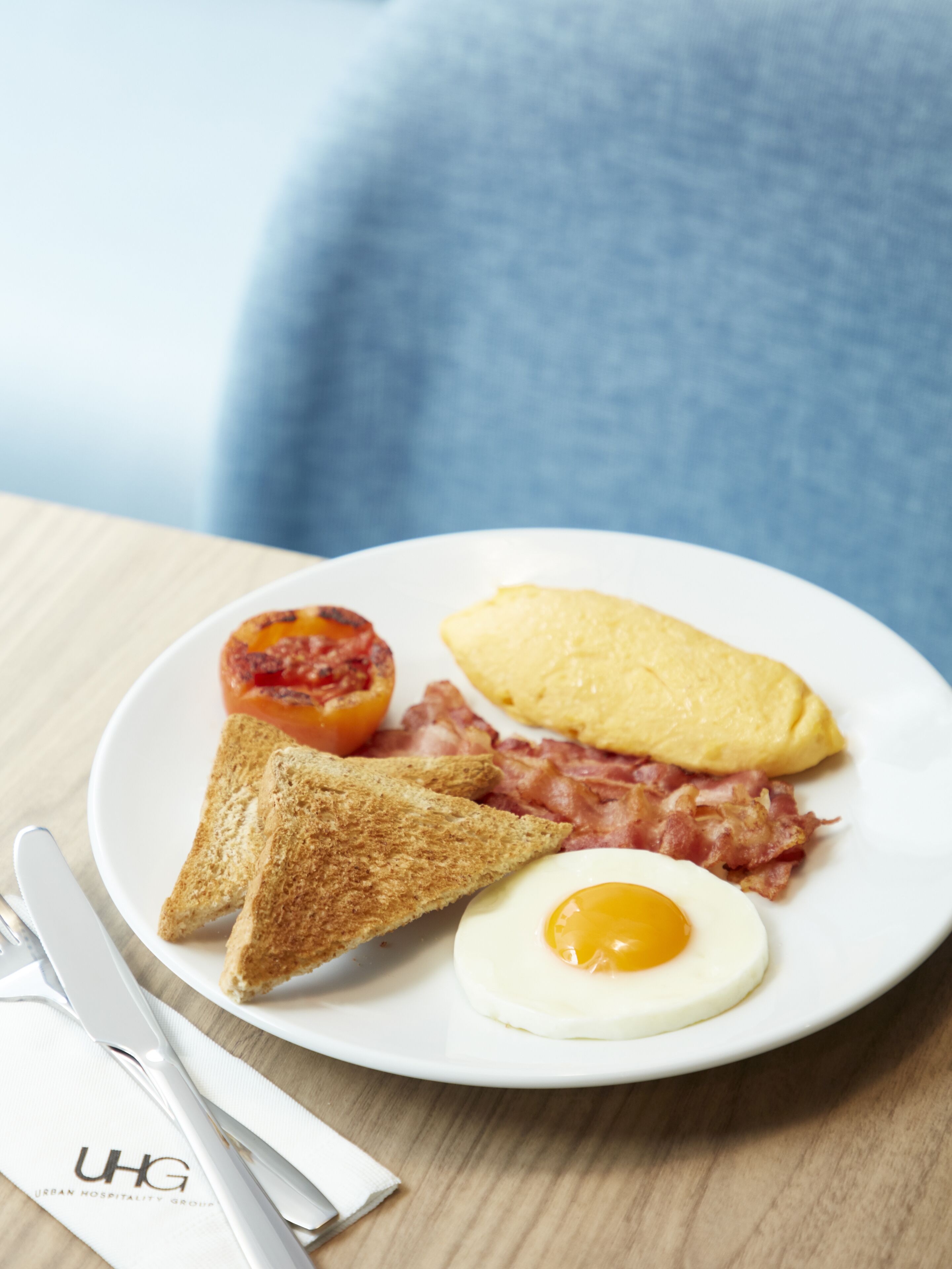 A plate with toast, bacon, an egg, and a tomato on a white plate.