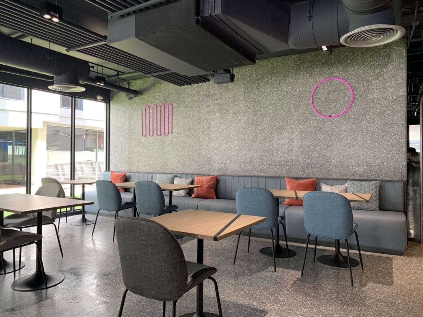 A modern cafe with a grey sofa, blue chairs, and tables.