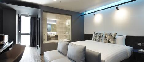 Una habitación de hotel moderna con una cama grande, un sofá, un escritorio y un baño visible a través de una puerta abierta.