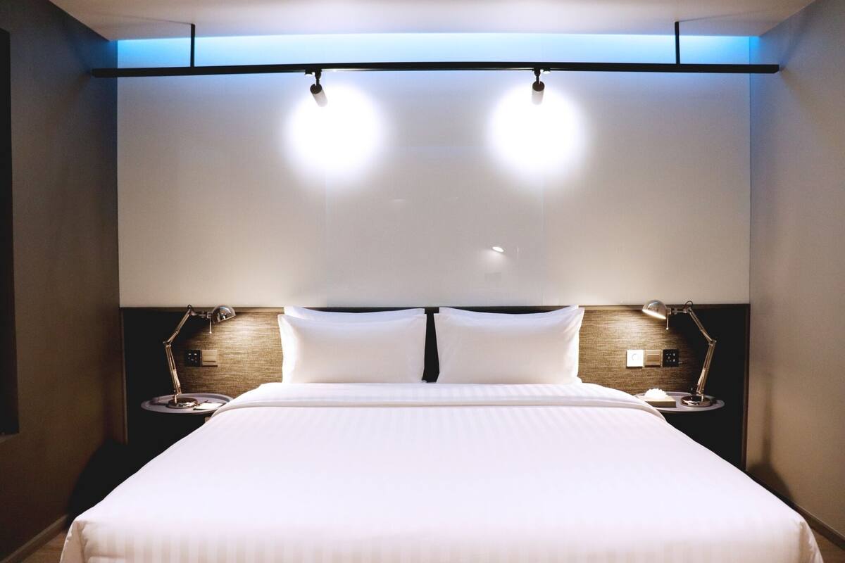 A hotel room with a large bed, two bedside tables, and a headboard with integrated lighting.