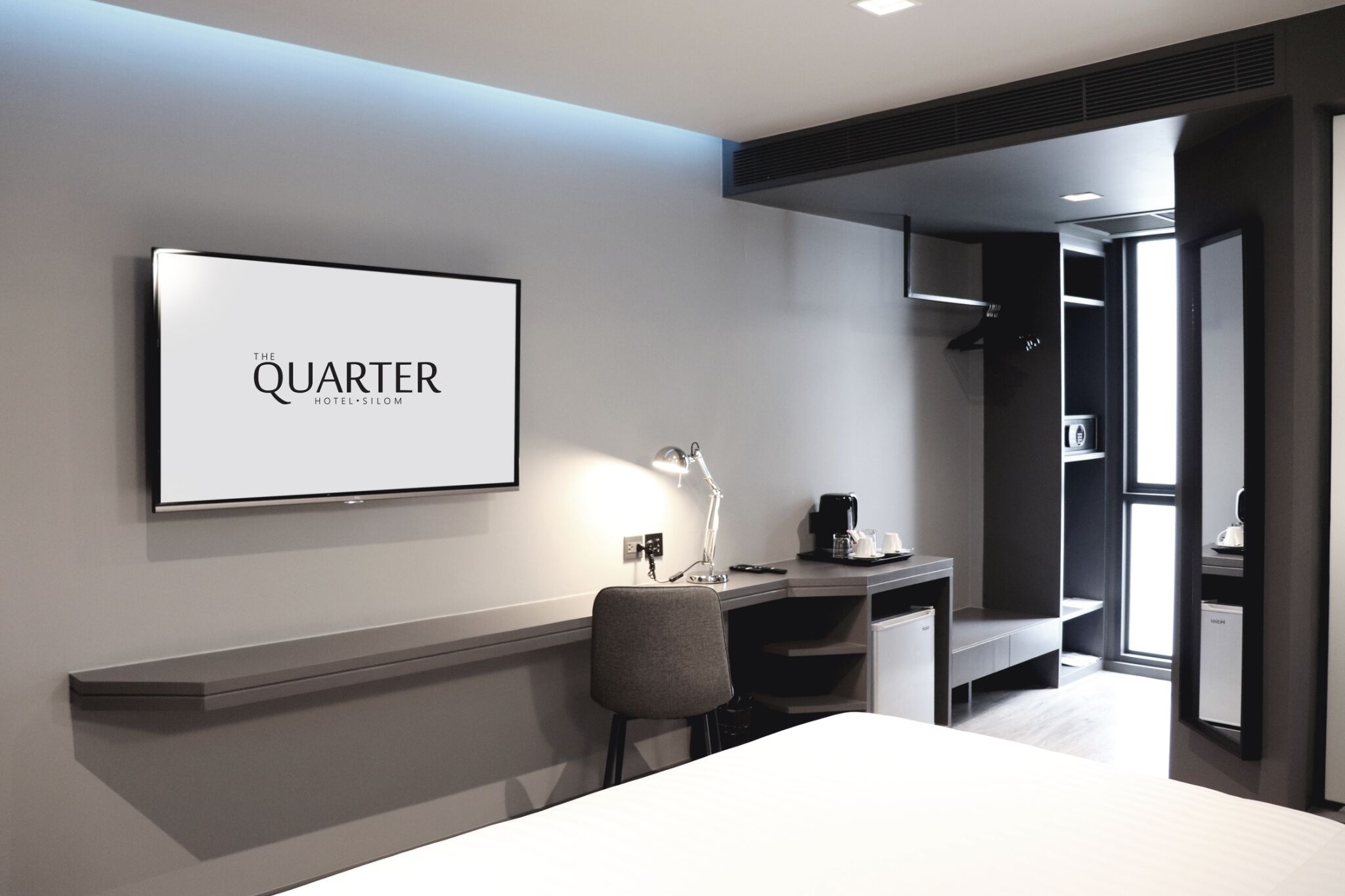 A modern hotel room with a bed, a desk with a chair, a desk lamp, a coffee maker, and a large framed sign on the wall.
