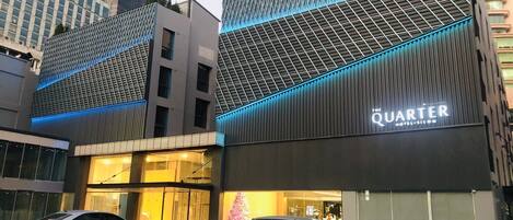 Ein modernes Hotel mit einem gut sichtbaren 'QUARTER' Schild, das eine rasterartige Fassade und blaue Lichtakzente aufweist.