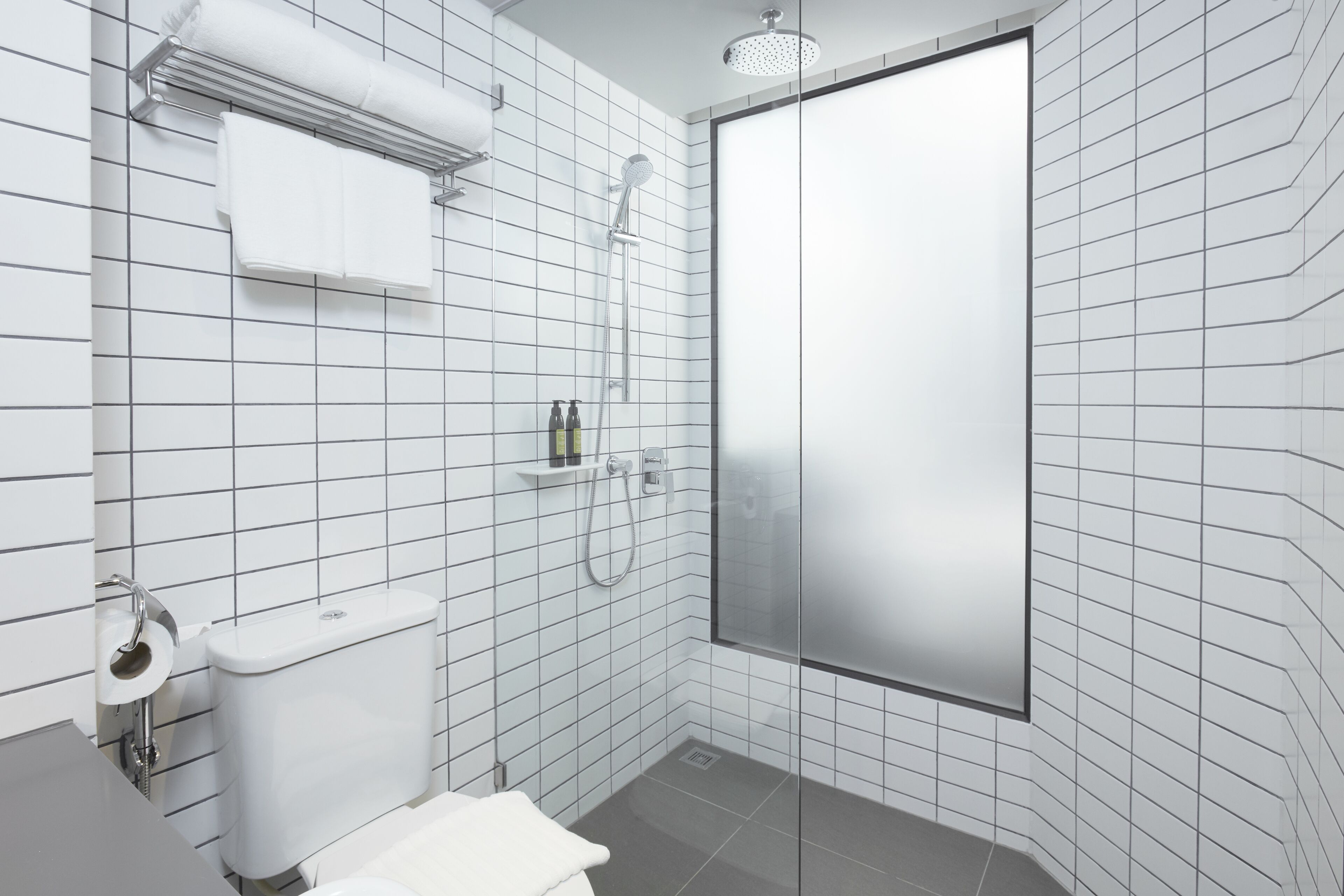 A modern bathroom with white tiled walls, a glass shower enclosure, a toilet, and a sink.