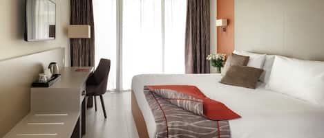 A hotel room with a bed, a desk, a chair, a TV, and a window with curtains.