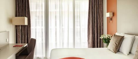 Una habitación de hotel con cama, escritorio, silla y lámpara.