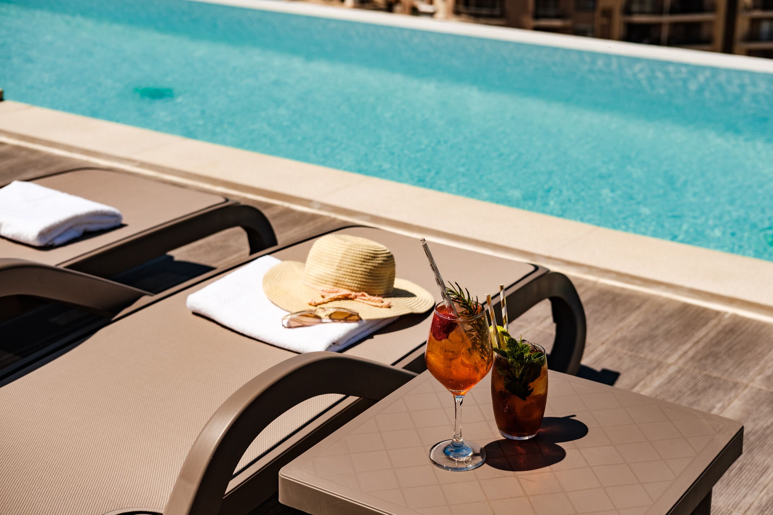 A poolside table with a drink, a hat, and a towel.