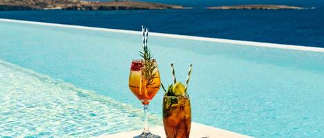 A poolside setting with two drinks, one in a glass and one in a tumbler, with a clear view of the sea and distant land in the background.