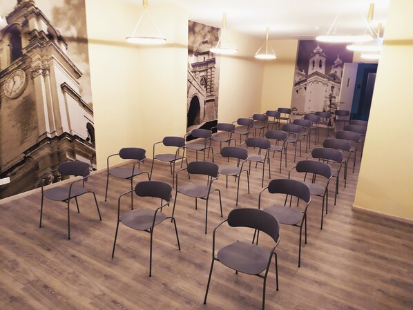 Un salón de conferencias con filas de sillas, piso de madera y un mural de un edificio en la pared.