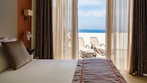 Habitación de hotel con cama, planta en maceta, escritorio y vista a la playa.