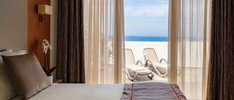 Une chambre d’hôtel avec un lit, une plante en pot, un bureau et une vue sur la plage.