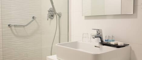 Un baño moderno con un lavamanos blanco, un cabezal de ducha manual y un espejo sobre el lavamanos.
