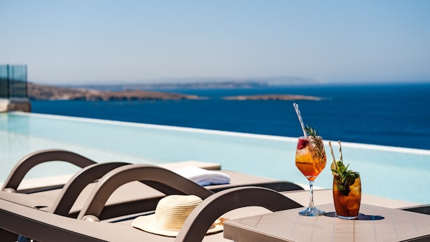 Mesa junto a la piscina con dos bebidas y una pajita, con vistas a un mar azul y despejado.