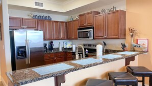A modern kitchen with wooden cabinets, a stainless steel refrigerator, a microwave, and a granite countertop.