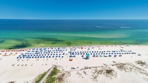 Luchtbeeld van een strand met talloze parasols en ligbedden, een heldere blauwe zee en een zandstrand.