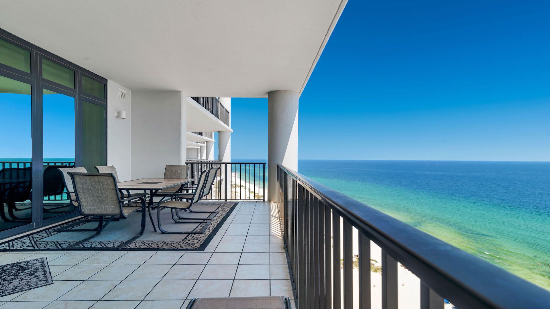 Un balcon avec vue sur l’océan, une table à manger avec des chaises et un sol carrelé.