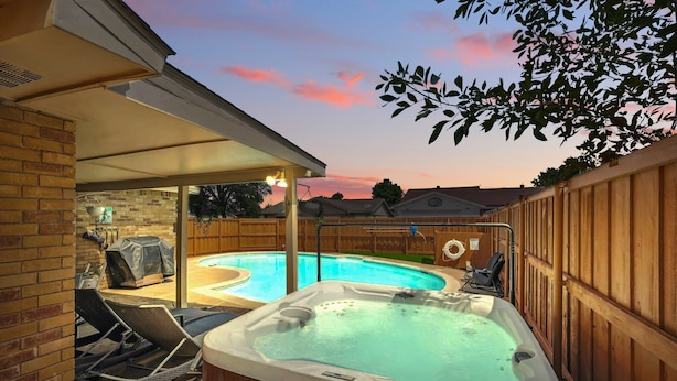 A backyard with a hot tub, a covered patio, and a swimming pool.