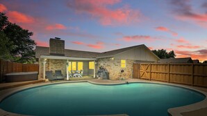 A backyard with a swimming pool, a hot tub, and a covered patio area.