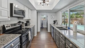 A modern kitchen with white cabinetry, a stainless steel microwave, a built-in oven, granite countertops, and a ceiling light fixture.